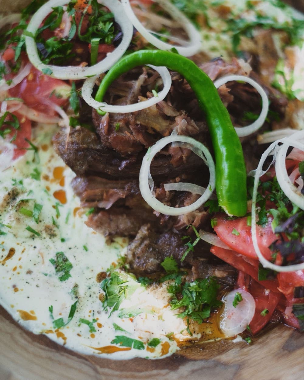 Блюдо национальной кухни: тушёное мясо с помидорами, луком, зеленью и острым перцем в деревянной чаше