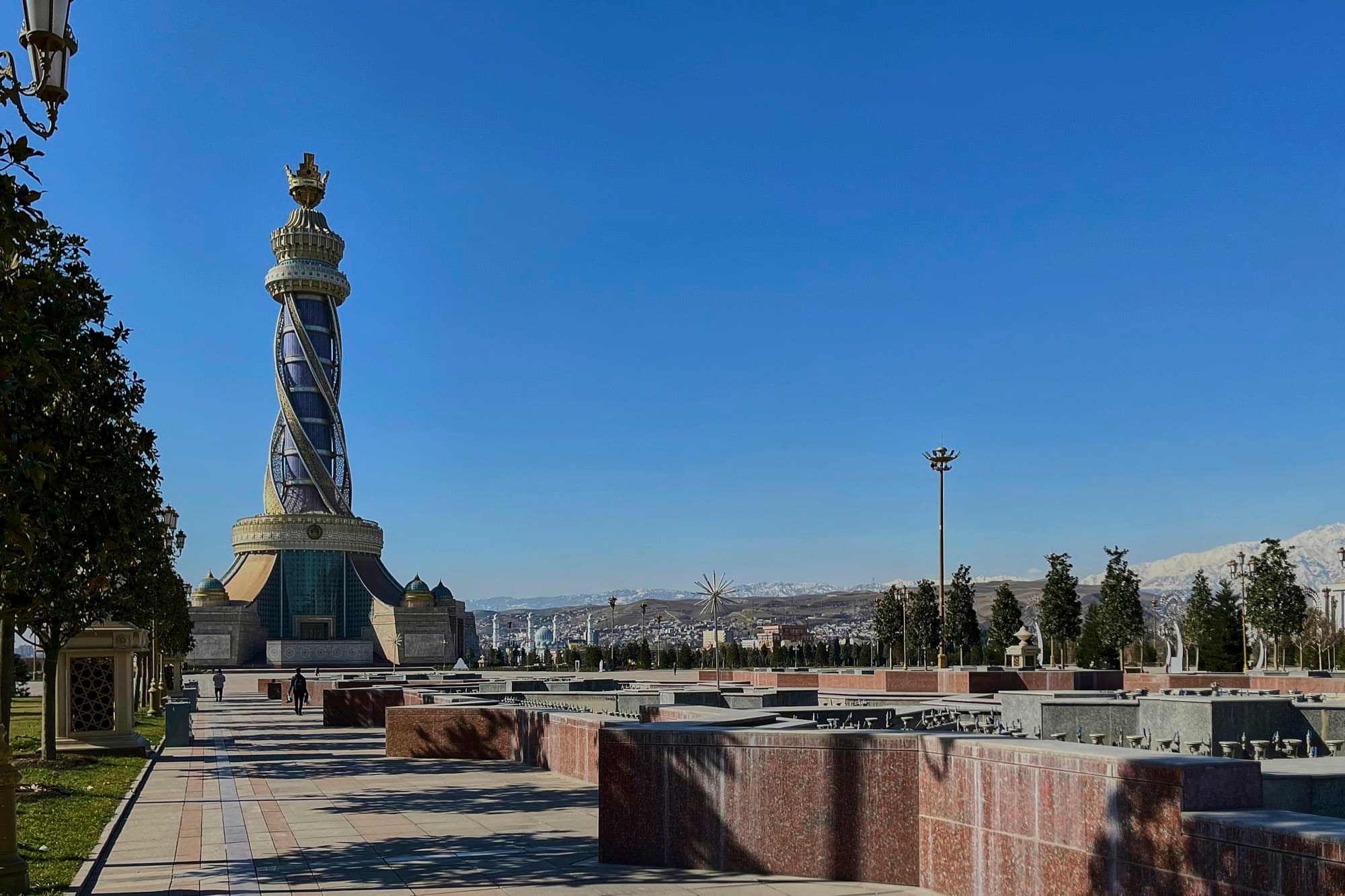 Монумент «Истиклол» и площадь с фонтанами в Душанбе, вдали горы